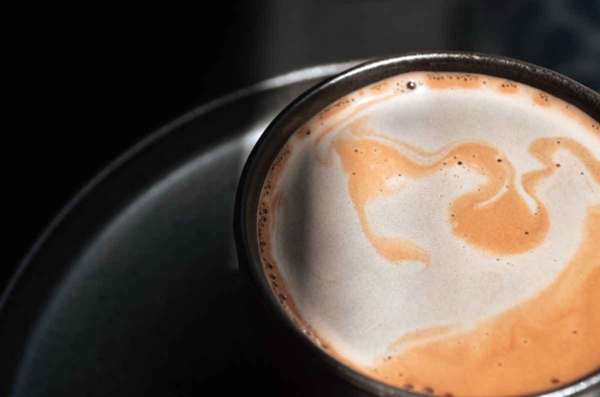 A cappuccino with latte art in a dark ceramic cup, shot close on a near-black plate
